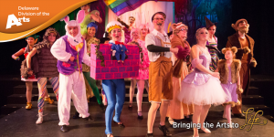 Delaware Division of the Arts orange logo banner over an image of male and female actors of different ages on stage in fairy tale character costumes from Clear Space Theatre Company